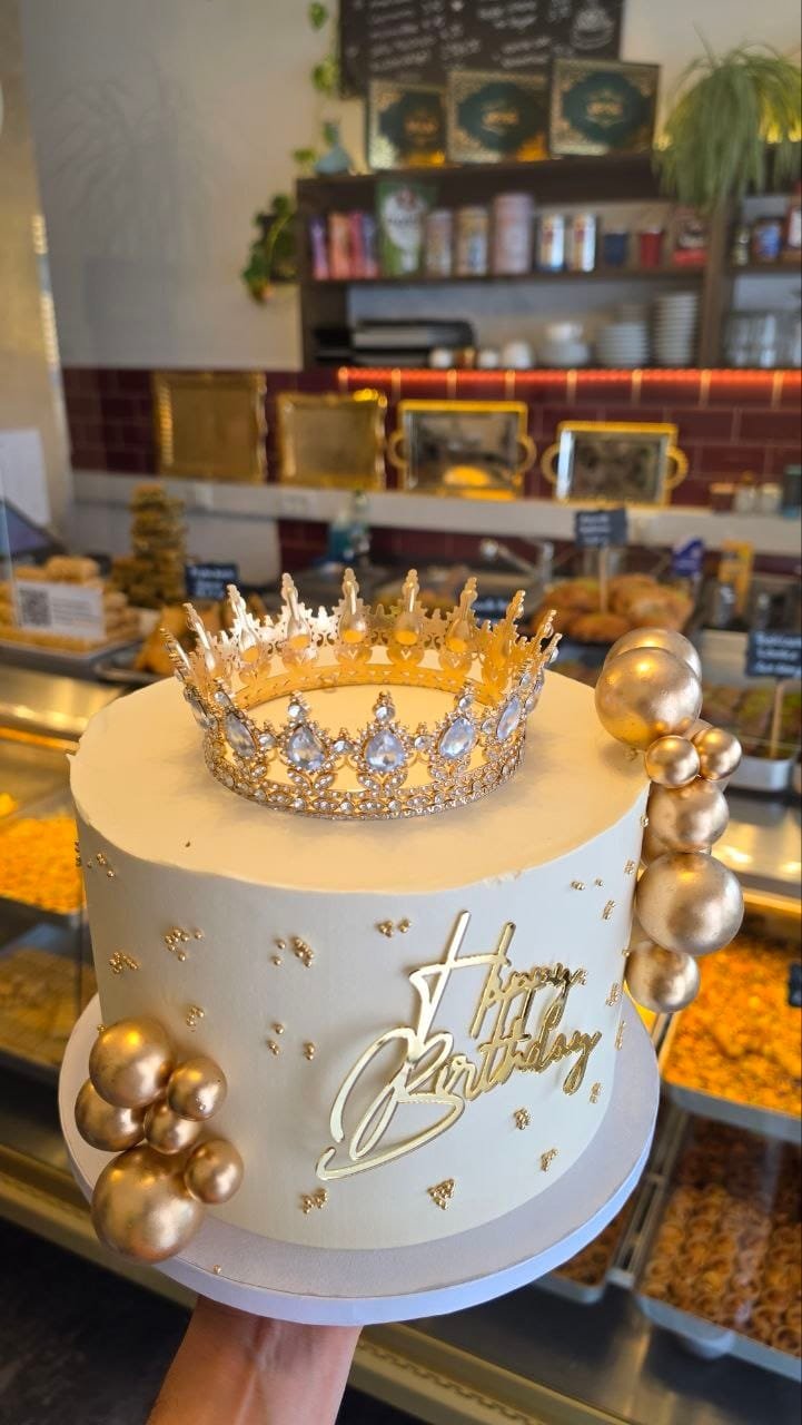 Cremefarbene Geburtstagstorte mit goldener Krone und Happy-Birthday-Topper